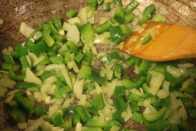green bell pepper and onions in dutch pot with wooden spatula sticking out