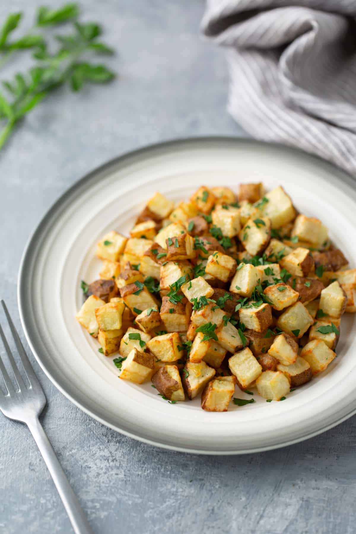 roasted potatoes in white plate with for on side