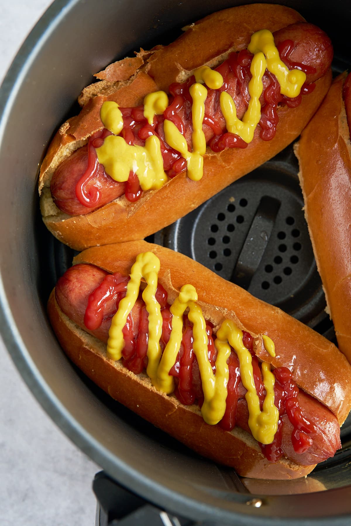 air fryer hot dogs in air fryer basket covered in ketchup and mustard
