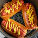 hot dogs in buns in air fryer basket topped with ketchup and mustard