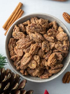 candied pecans in a bowl with cinnamon stick and pinecone around it