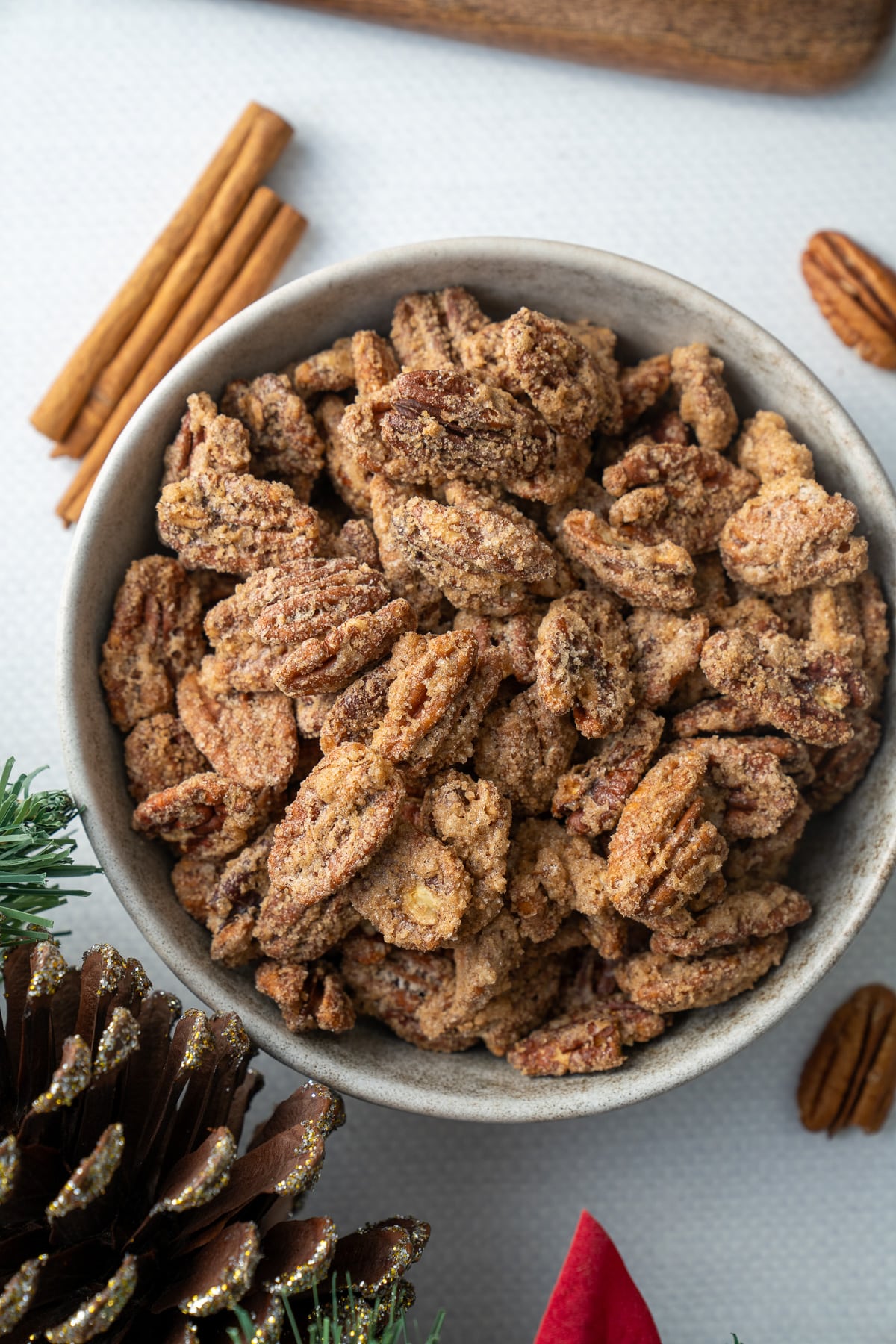 candied pecans in a bowl with cinnamon stick and pinecone around it