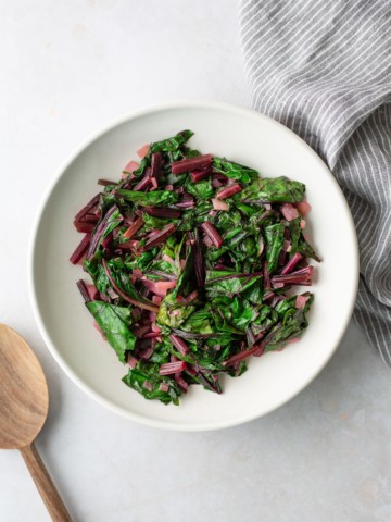 sauteed beet greens in white plate with spoon on side