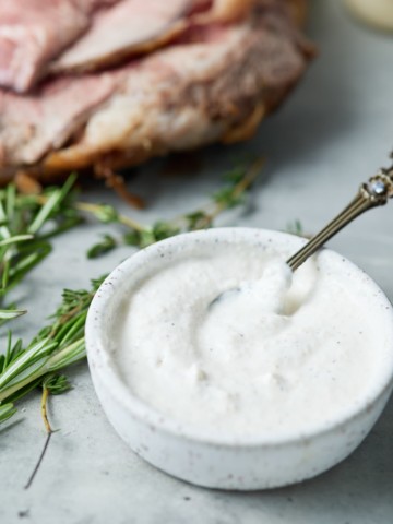 Close up of horseradish sauce in a bowl net to fresh herbs.