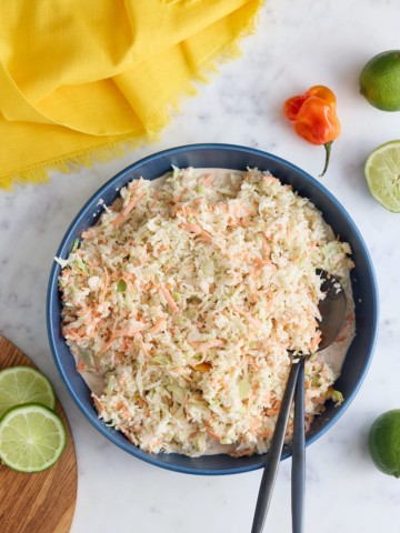 A bowl of Jamaican coleslaw with serving spoons.