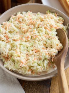 Coleslaw in a serving bowl with a wooden spoon.