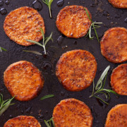 Close up image of baked sweet potato rounds on a baking sheet with springs of fresh rosemary.