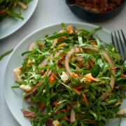 A white plate of fresh collard green salad with a bowl of bacon vinaigrette set alongside.