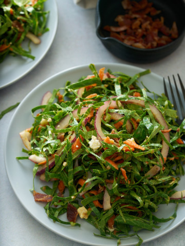 A white plate of fresh collard green salad with a bowl of bacon vinaigrette set alongside.