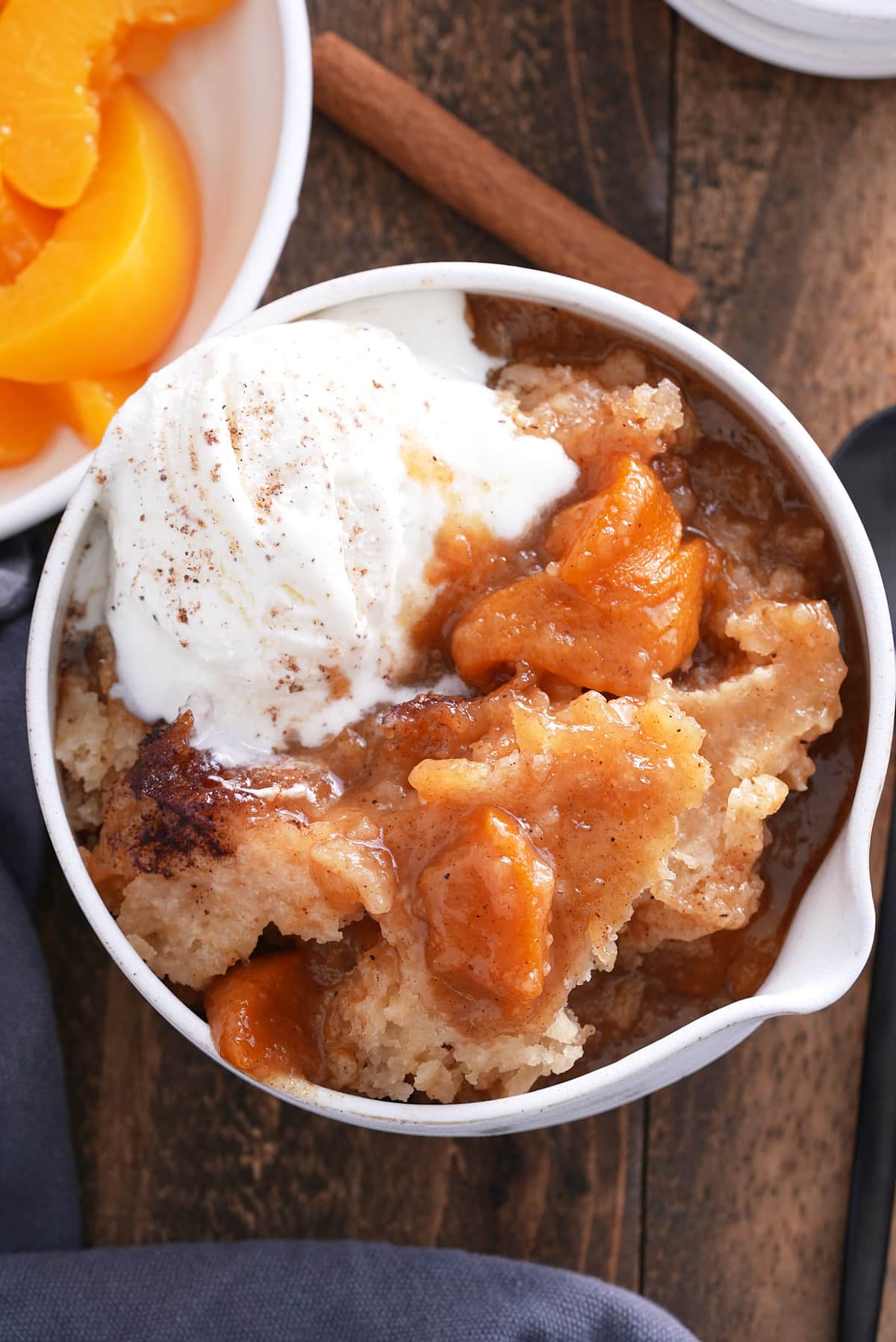A serving of peach cobbler in a white bowl with ice cream.