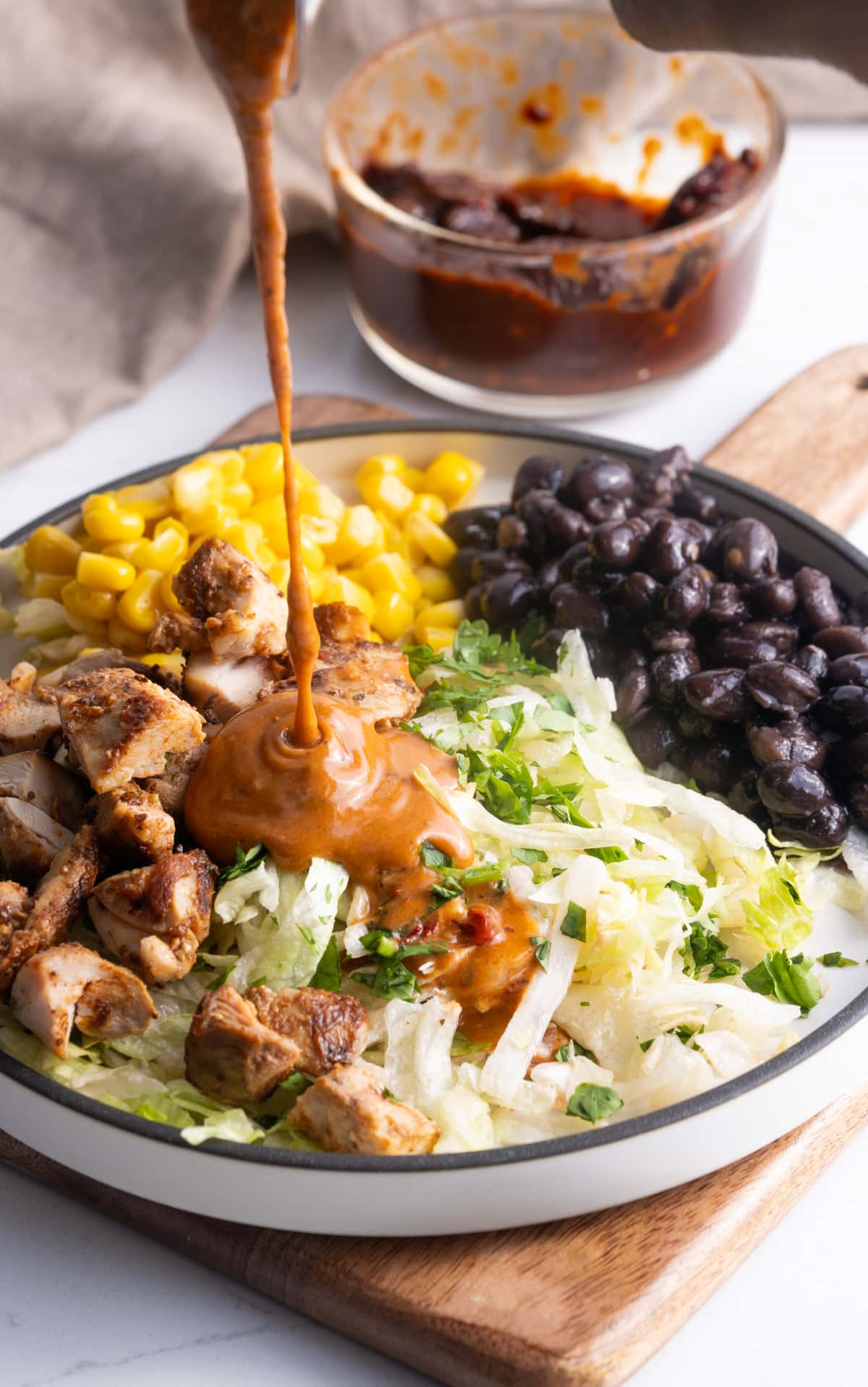 vinaigrette being poured over salad with chicken, lettuce, corn, and black beans