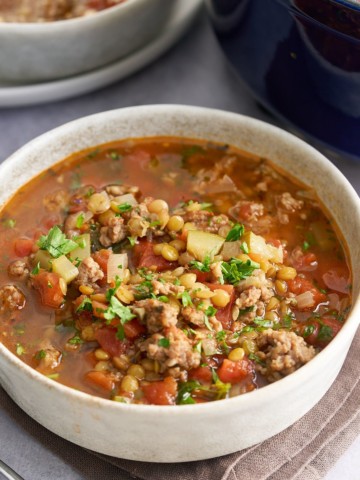 A bowl of sausage lentil soup garnished with some freshly chopped parsley.