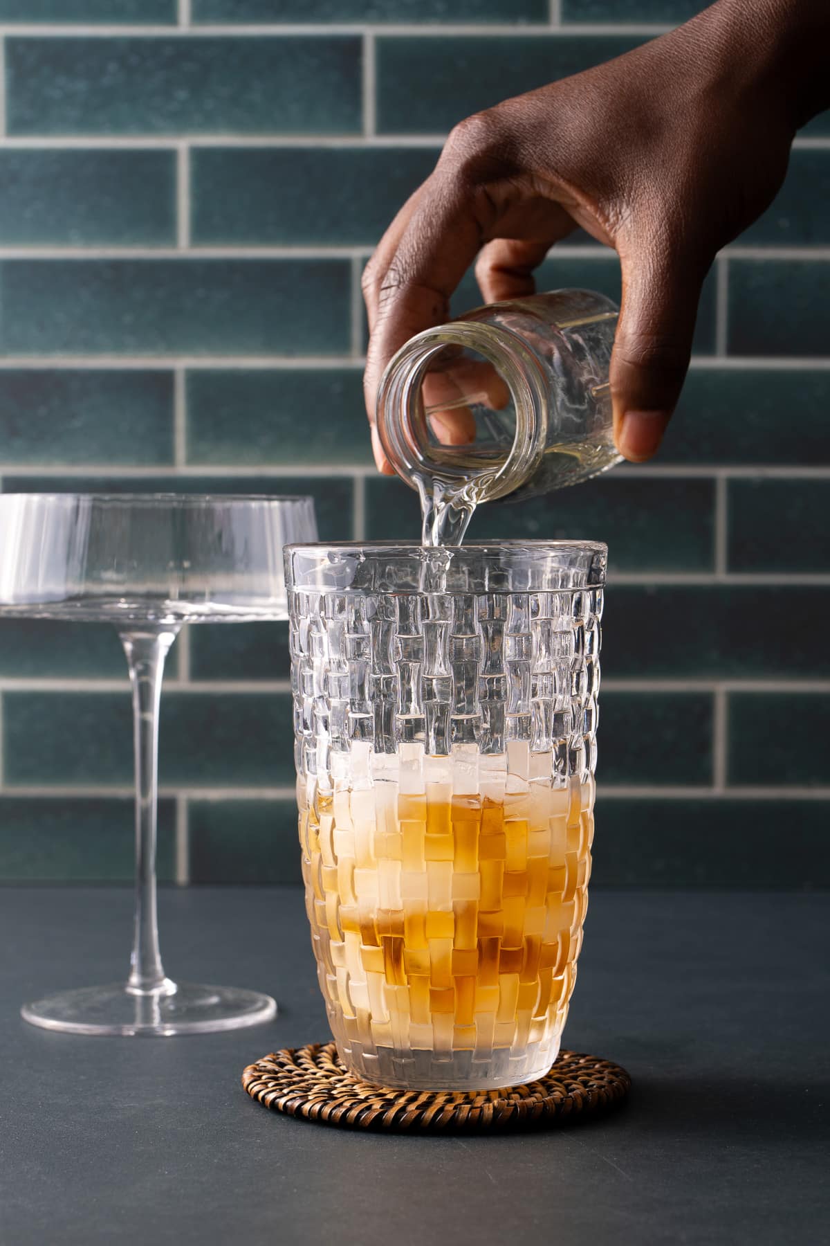 liquor being poured into a cocktail shaker that has ice