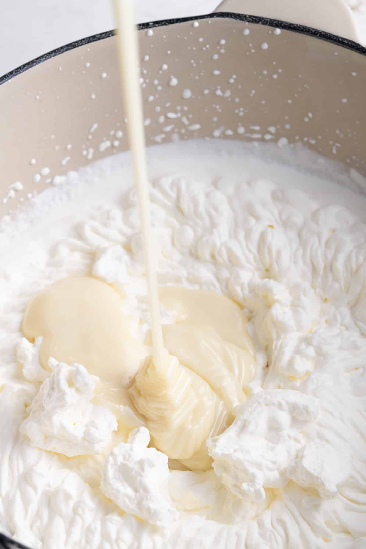sweetened condensed milk being poured into whipped heavy cream
