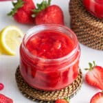 strawberry compote in glass jar with strawberries and lemon in background