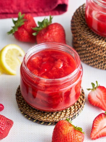 strawberry compote in glass jar with strawberries and lemon in background