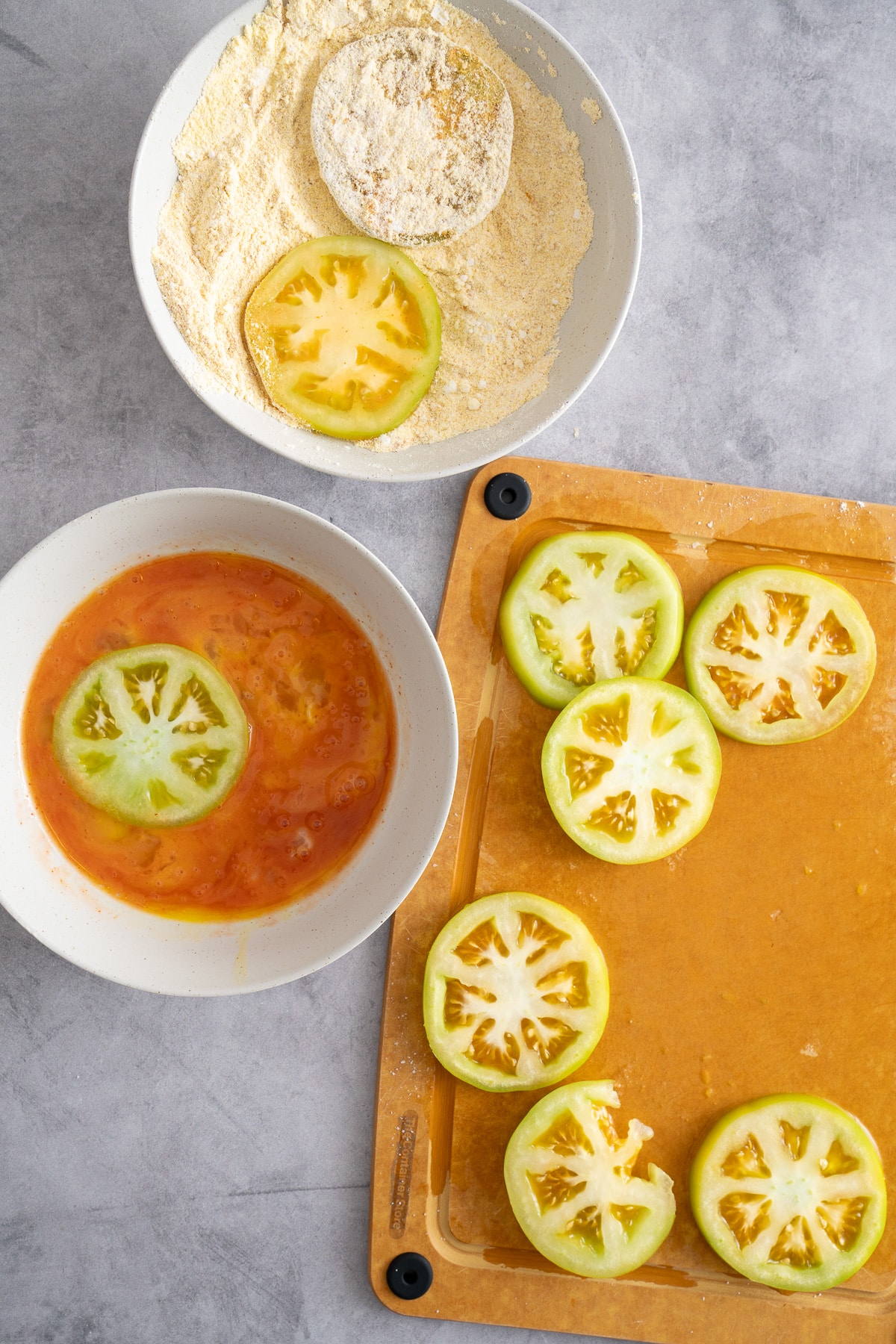 sliced green tomatoes om board, in hot sauce and egg mixture, and cornmeal and flour mixture