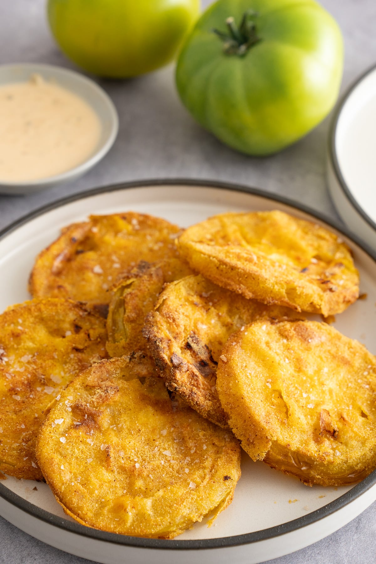 air fryer fried green tomatoes on white plate with green tomatoes in back