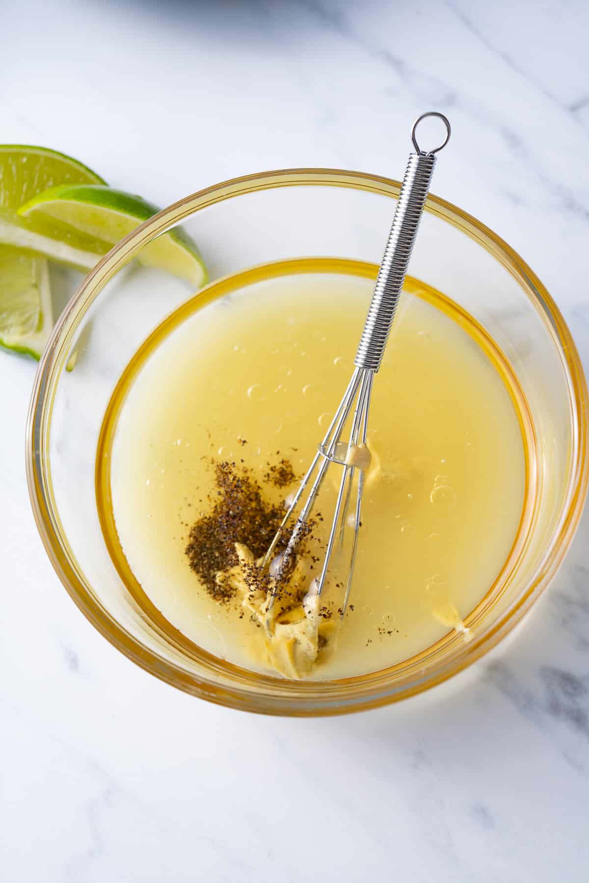 ingredients for lime vinaigrette in bowl with whisk inside