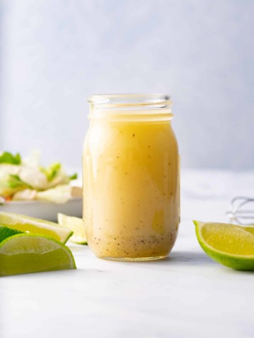 lime vinaigrette in glass bottle with limes and salad around it