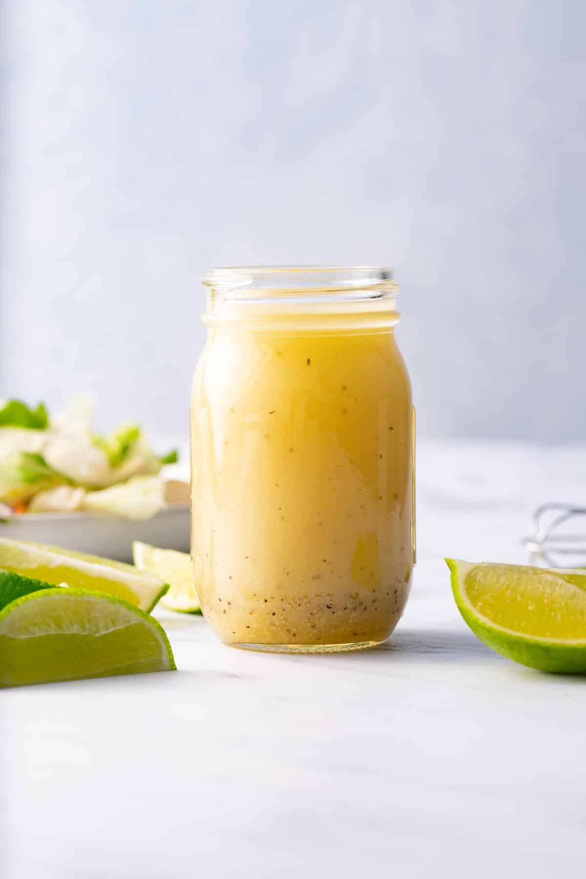 lime vinaigrette in glass bottle with limes and salad around it