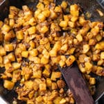 smothered potatoes in cast iron skillet with wooden spatula sticking out