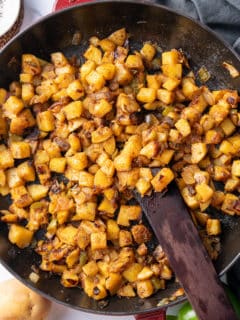 smothered potatoes in cast iron skillet with wooden spatula sticking out