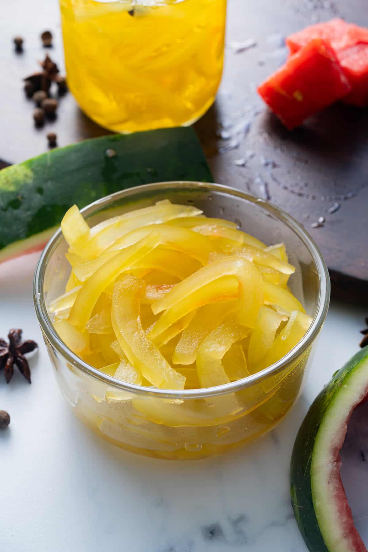 pickled watermelon rind in glass container with watermelon peel on side