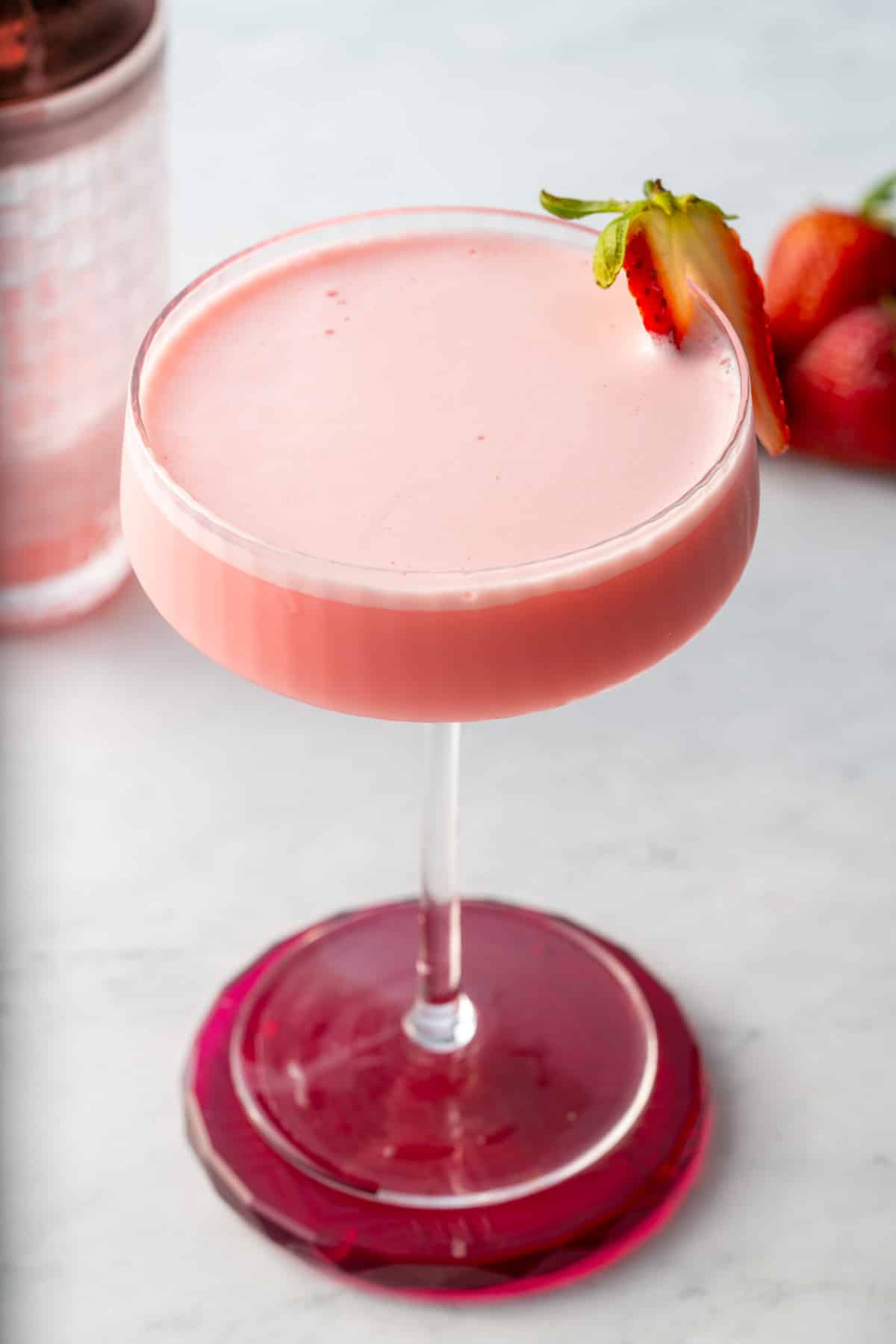 pink lady cocktail in glass with strawberry slice on side