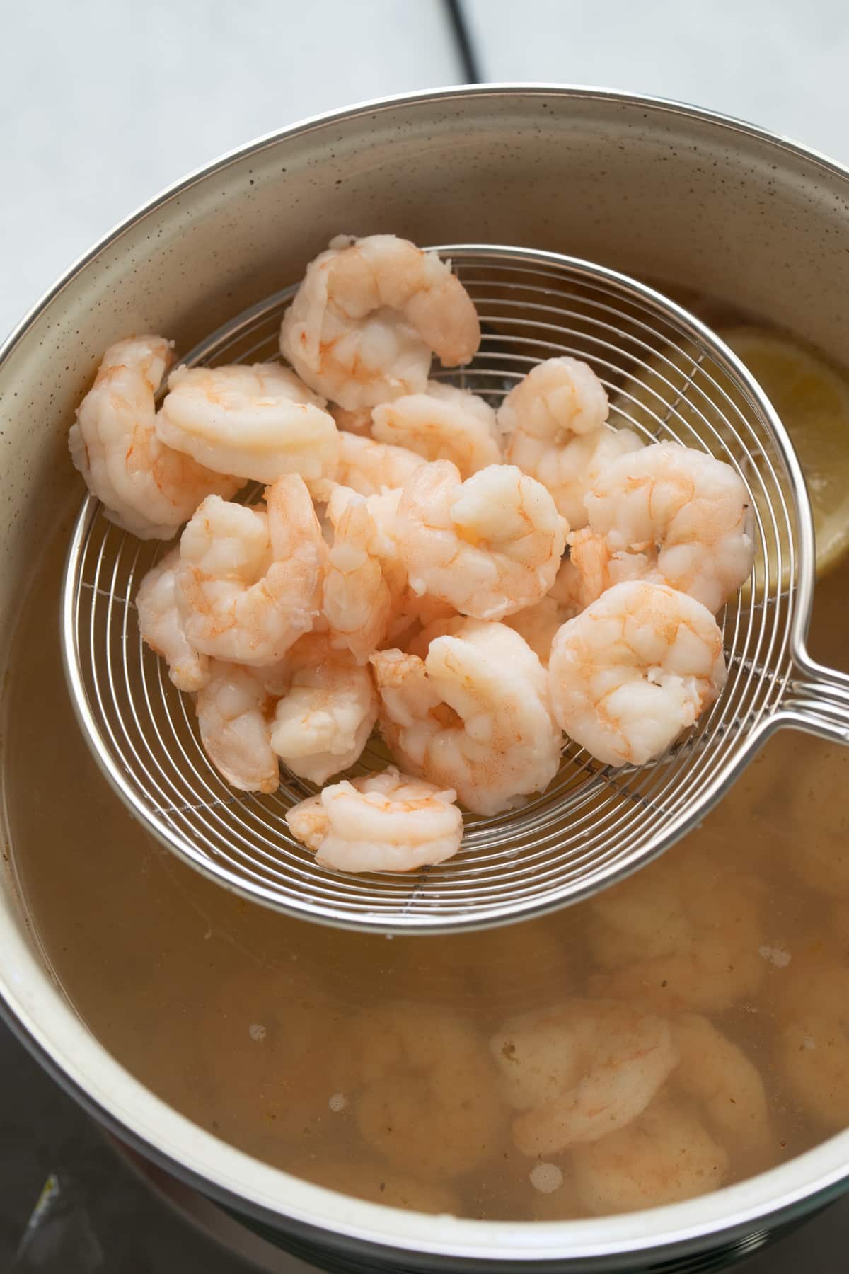 shrimp being picked up out of poaching liquid