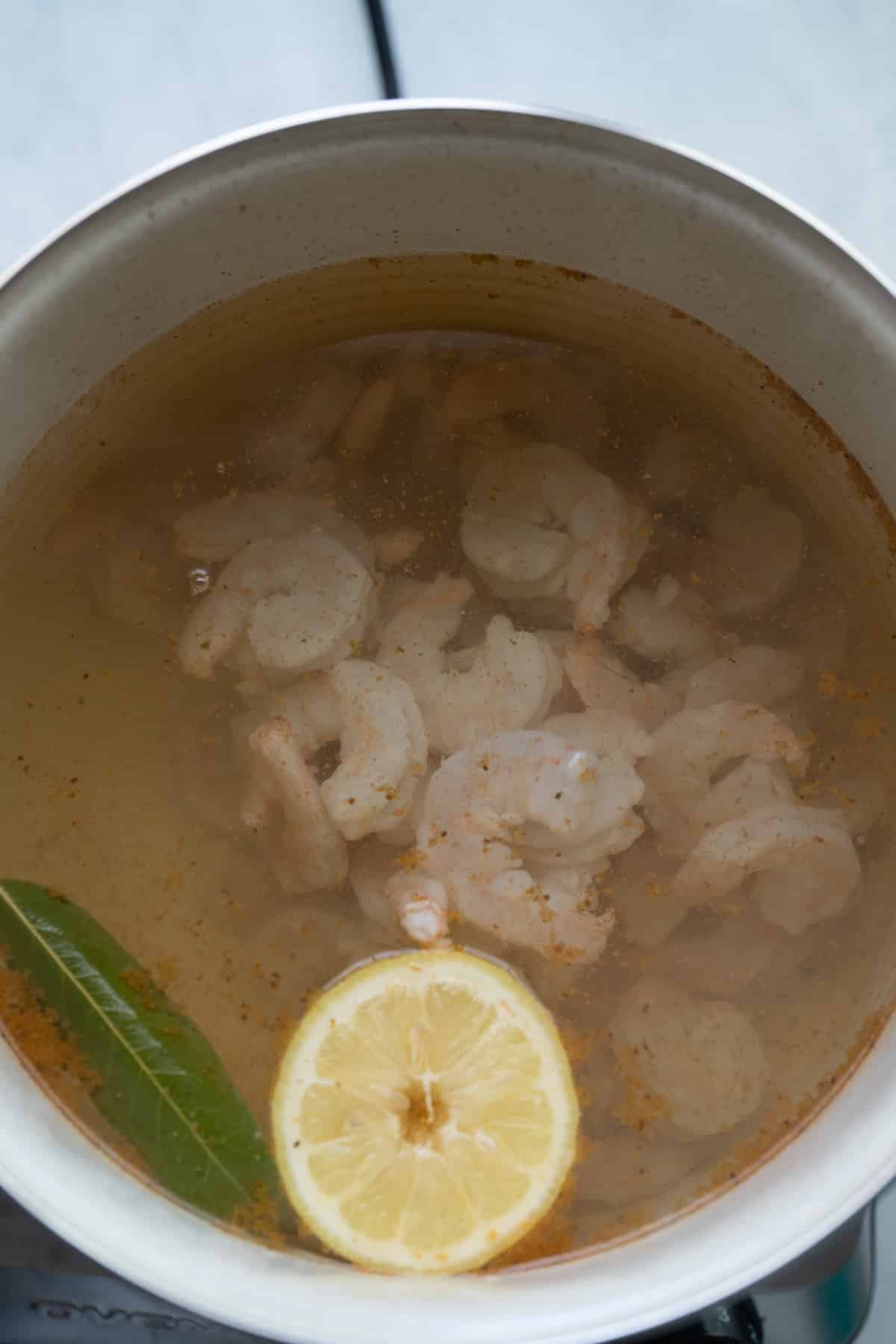 shrimp being poached in water with lemon and seasoning