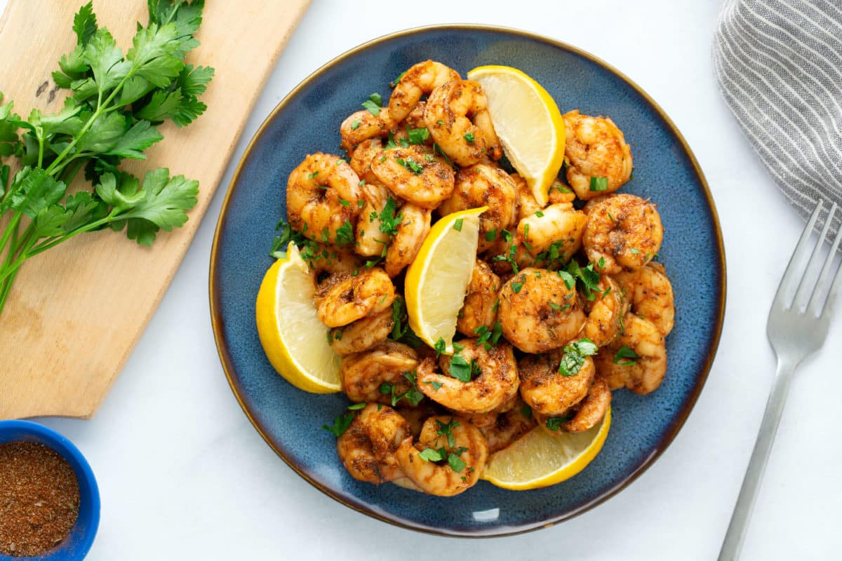 blackened shrimp on blue plate with fork on side with parsley on side