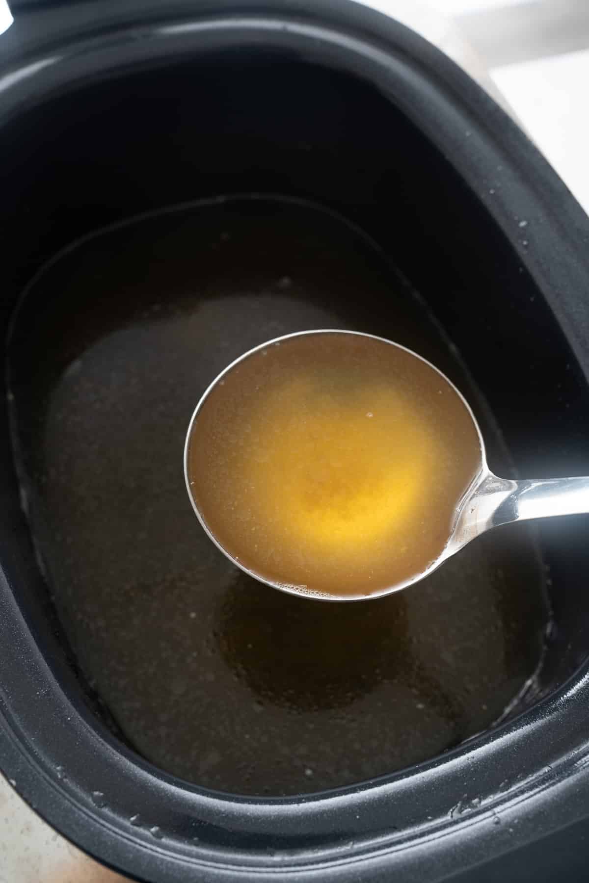 spoon picking up broth from the slow cooker