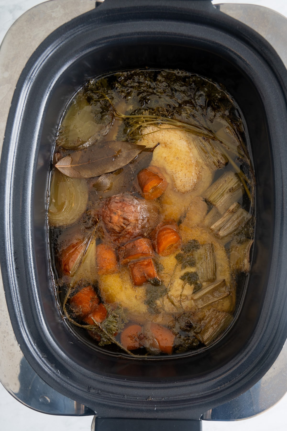 cooked chicken broth in slow cooker with vegetables and chicken still in slow cooker