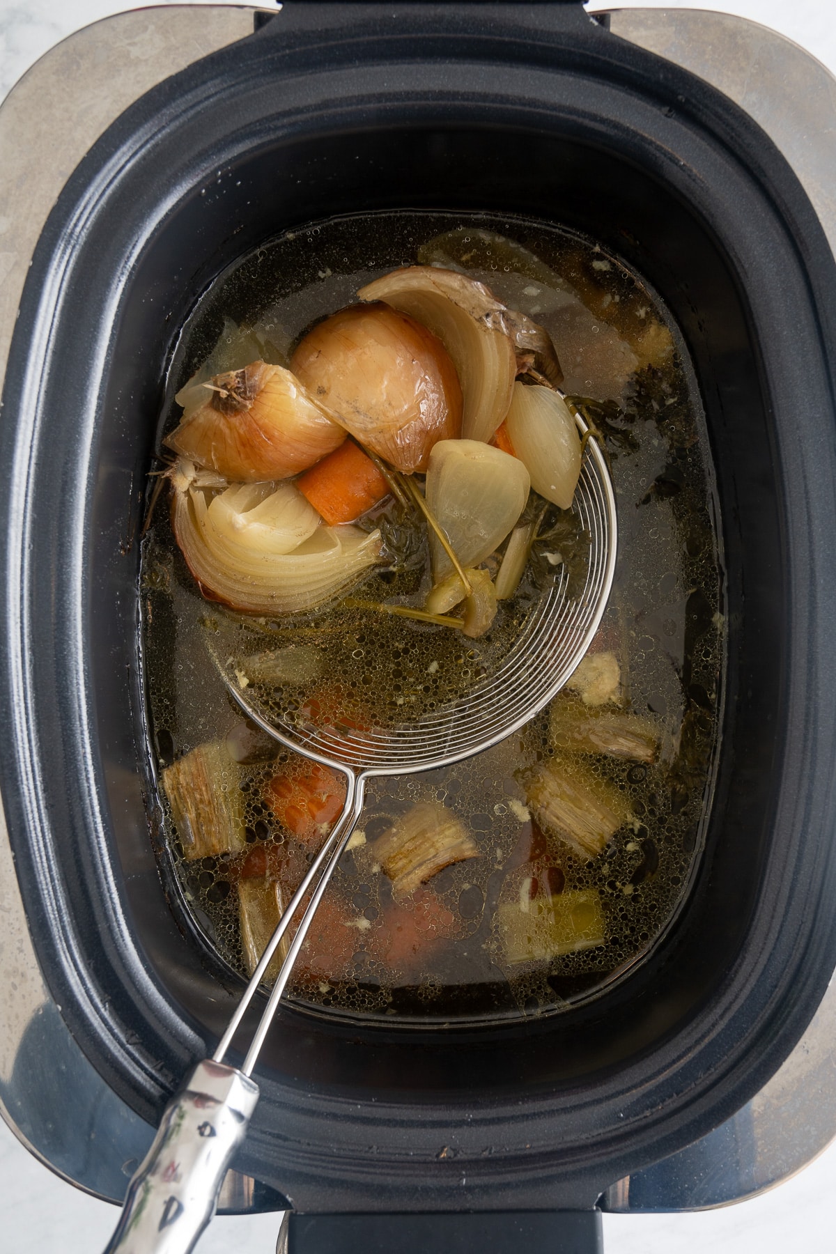 strainer taking out vegetables from the slow cooker broth