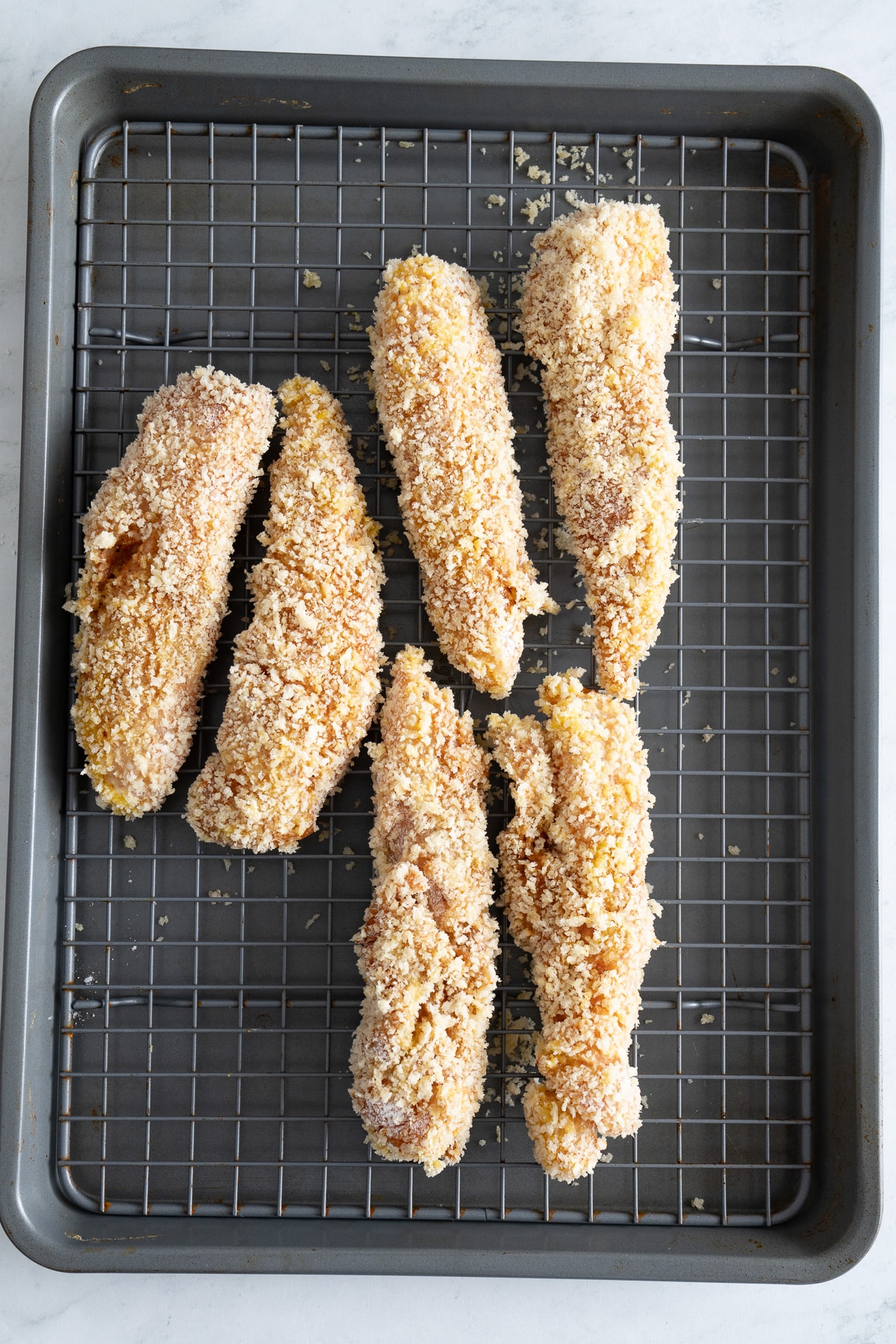 uncooked chicken tenders that are dredged on lined baking sheet with rack