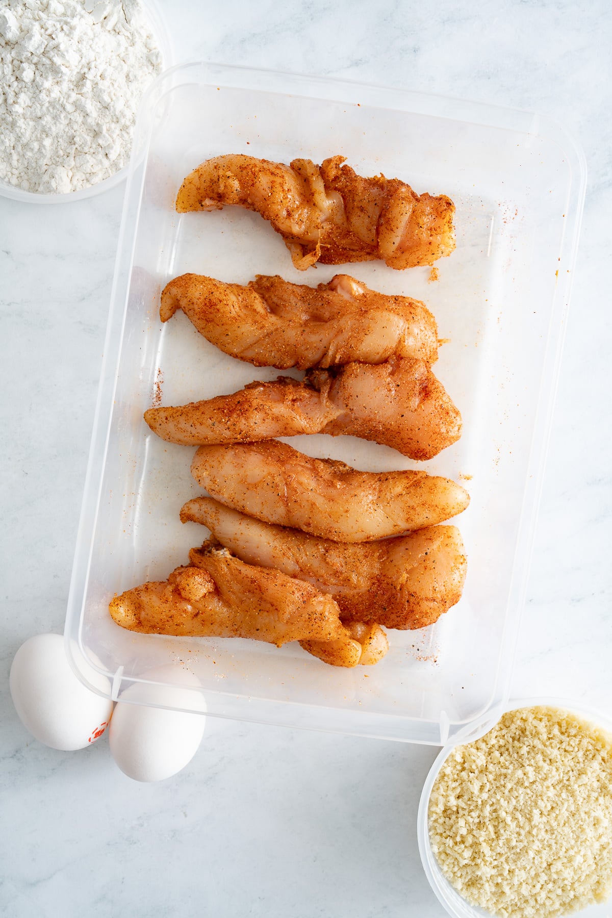 raw seasoned chicken tenders with eggs and panko and flour around them