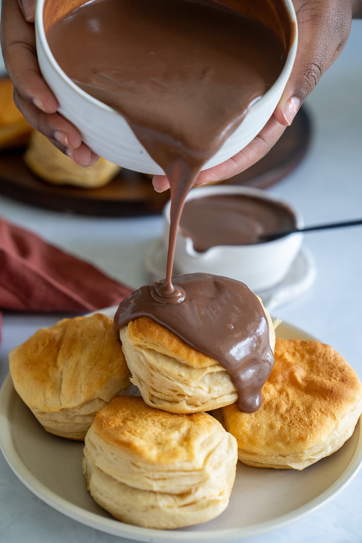 hands holding bold pouring chocolate gravy over biscuits