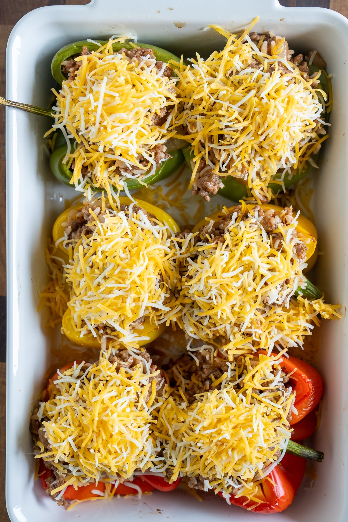 stuffed bell peppers in baking dish with unbaked cheese on top