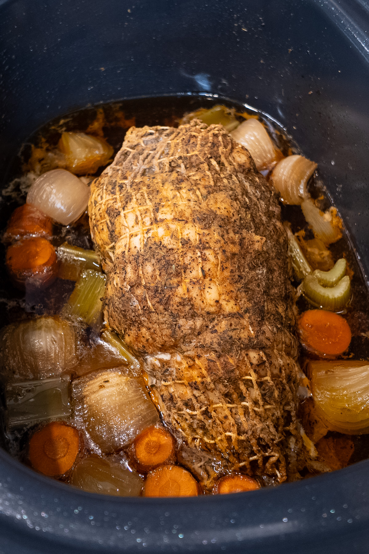 cooked turkey breast with net in slow cooker with onions, carrot, celery, and broth and drippings