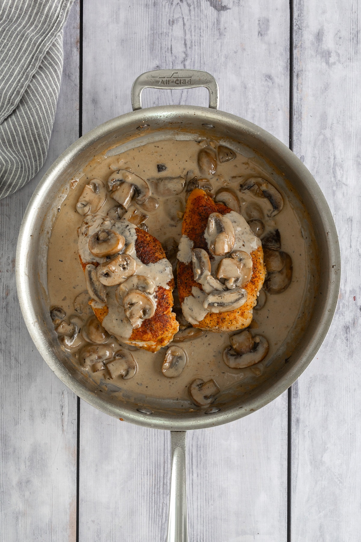 chicken breast in skillet covered in mushroom sauce