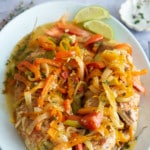 steamed fish covered in vegetables on white platter plate