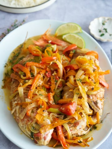 steamed fish covered in vegetables on white platter plate