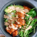 salmon bowl on table with cooked salmon, rice, greens, topping and sauce in bowl