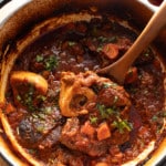 braised beef shanks in pot with spoon picking up beef shank