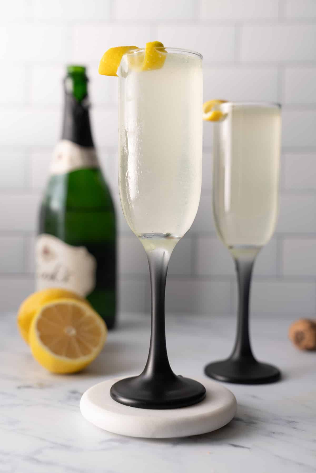 french 75 cocktail in glass with lemon garnish and champagne bottle in back