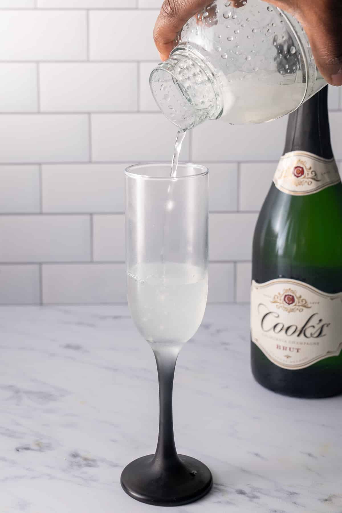 gin, sugar syrup, and lemon juice being poured into chilled champagne flute