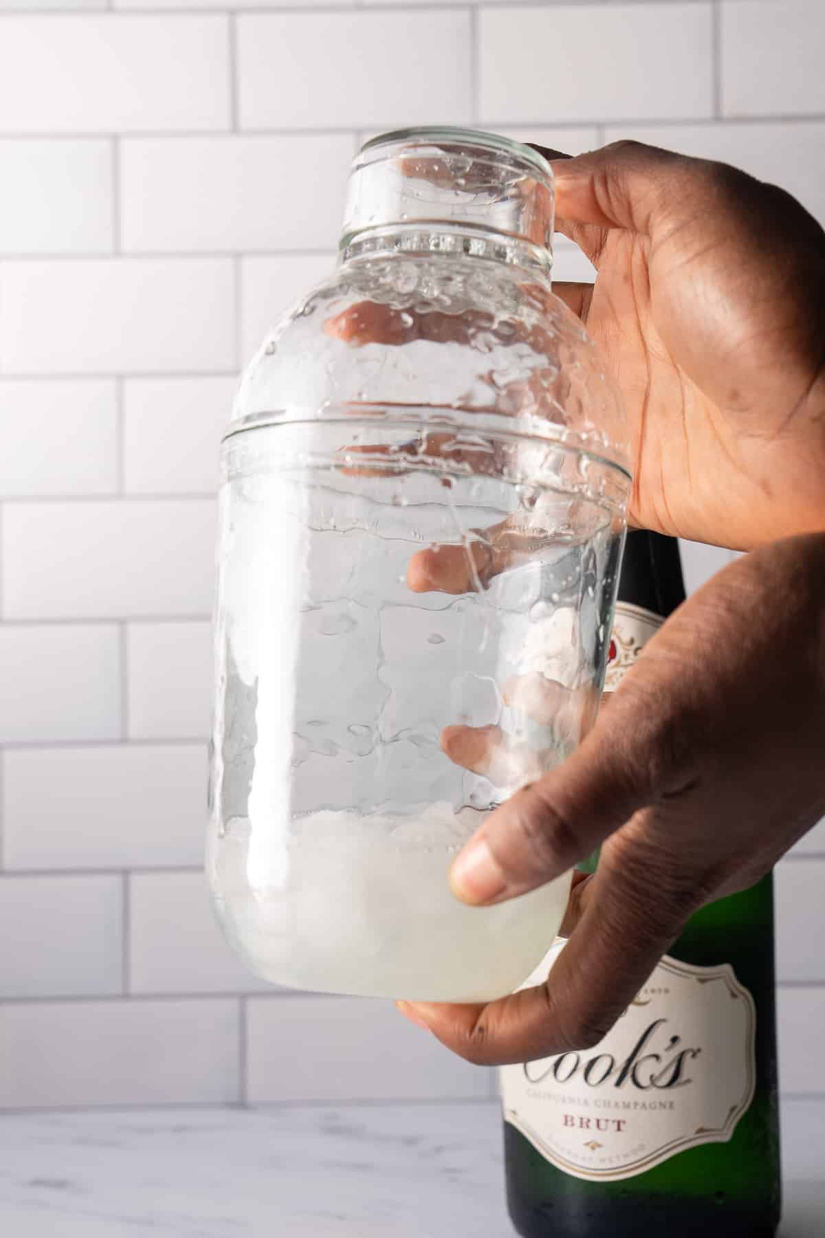 hands shaking cocktail shaker with ingredients in it