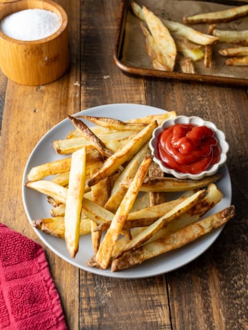 oven baked fries in plate with kecthup on side with red towel on side