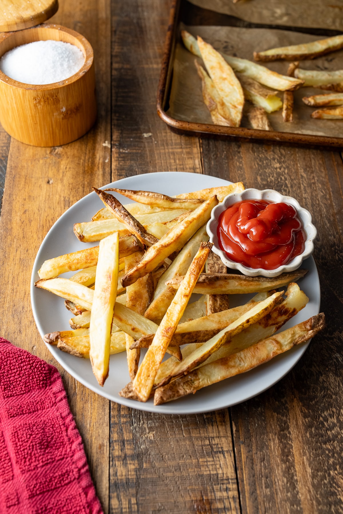 oven baked fries in plate with kecthup on side with red towel on side